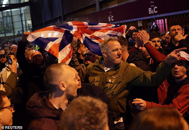 A crowd hold a Union Jack aloft outside the gates of Villa Park on a tempestuous night