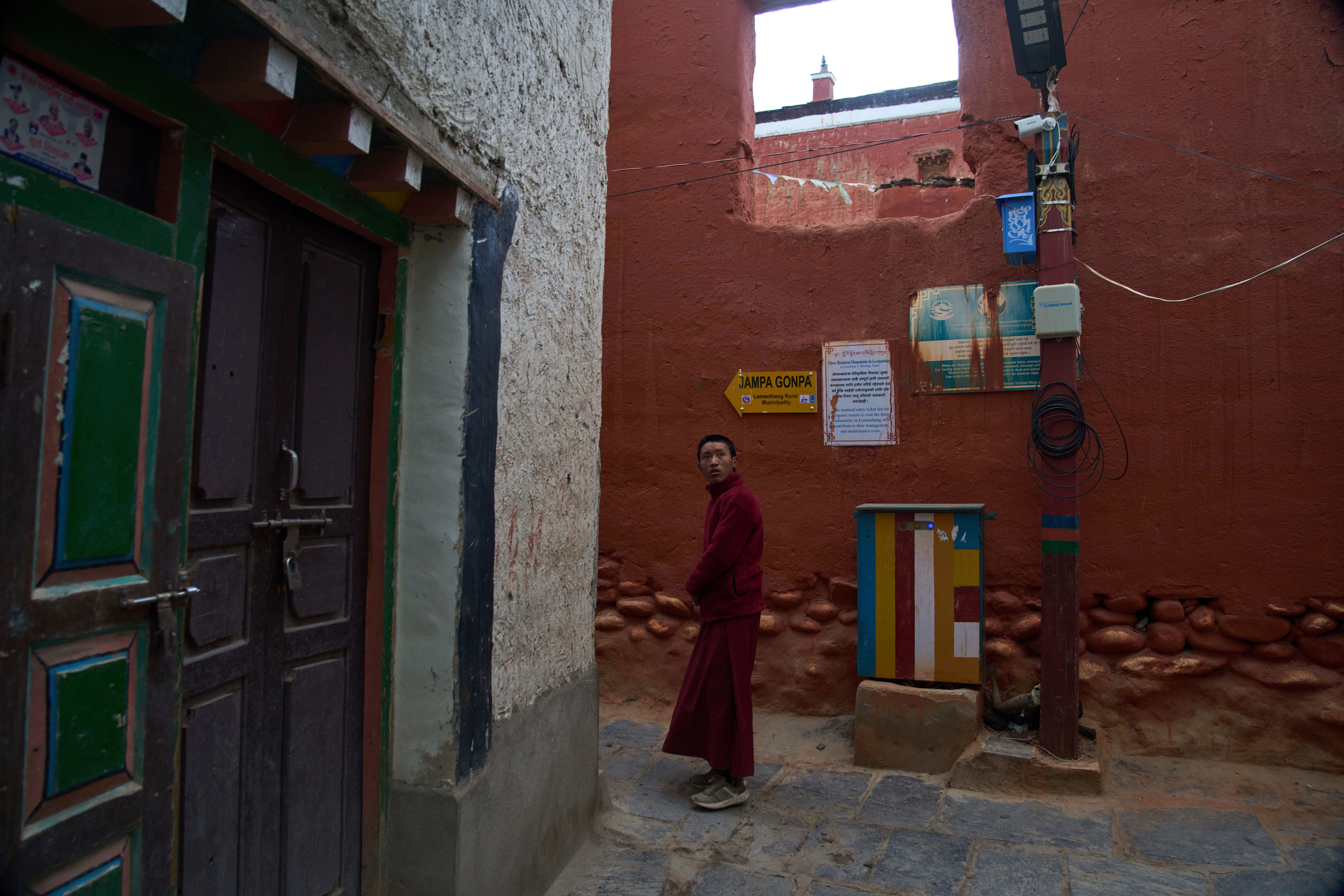 A Buddhist monk walks in an alley as a CCTV camera mounted on a pole watches over the area in the ancient ethnic Tibetan city of Mustang, Nepal