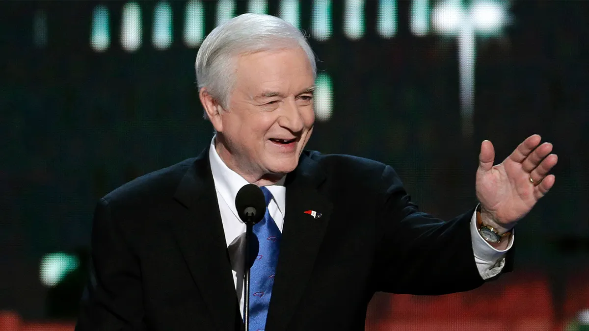 jim hunt u odijelu smiješeći se i mašući