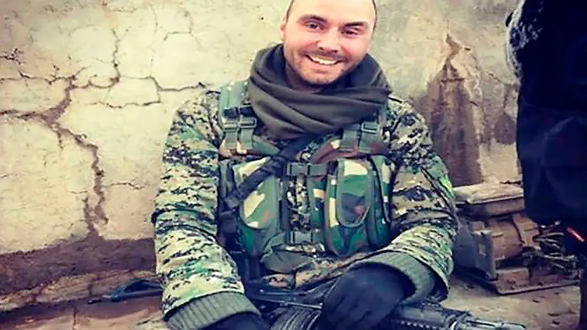 Čovjek u maskirnoj uniformi sjedi uz napukli zid i drži pušku.