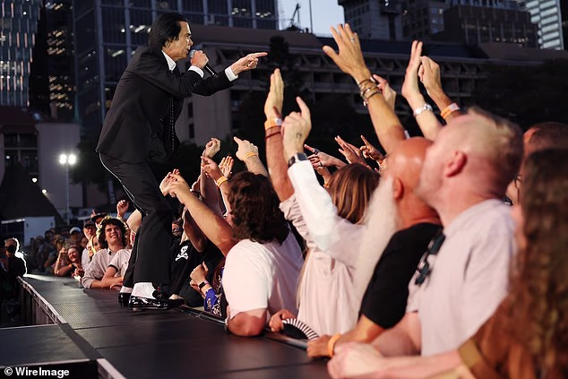 Odjeven u oštro crno odijelo i bijelu košulju, Cave je izgledao upečatljivo dok je koračao niz usku pistu koja se protezala duboko u gomilu, s mikrofonom u ruci, a njegova slobodna ruka ispružena da uhvati prste obožavatelja