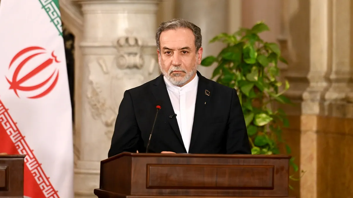 Iranski dužnosnik stoji za govornicom tijekom službene konferencije za novinare, s nacionalnim zastavama postavljenim iza njega.