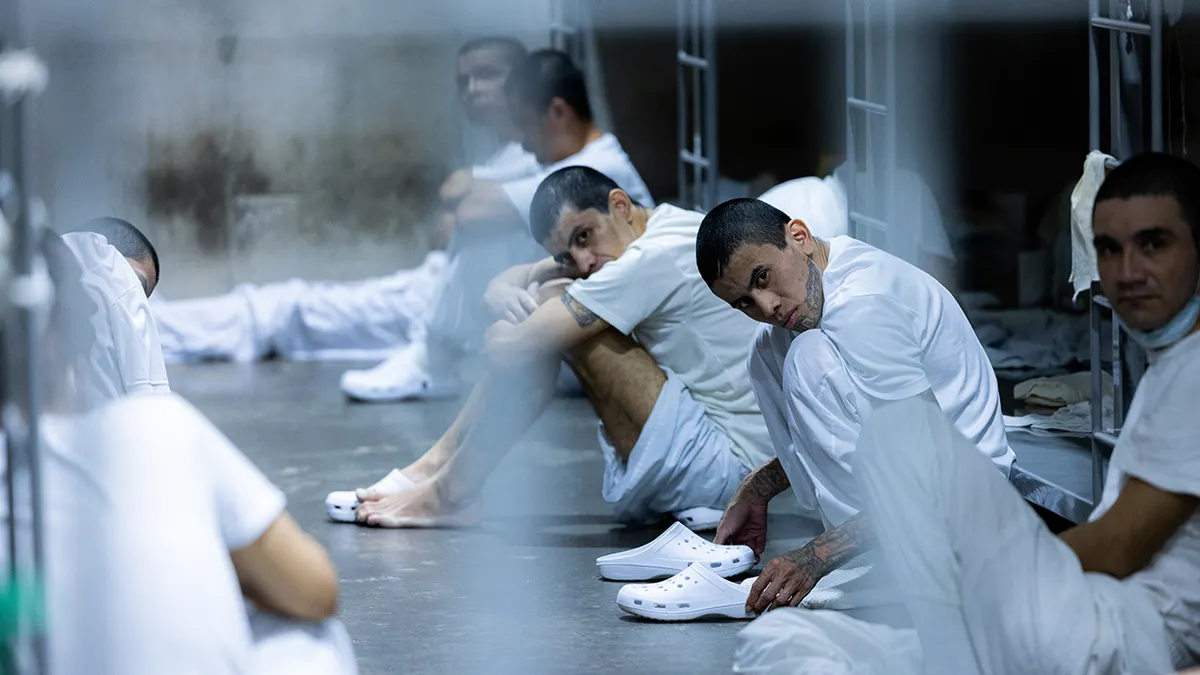 Članovi TDA u CECOT-u ​​sjede na tlu u bijelim uniformama i kroksicama