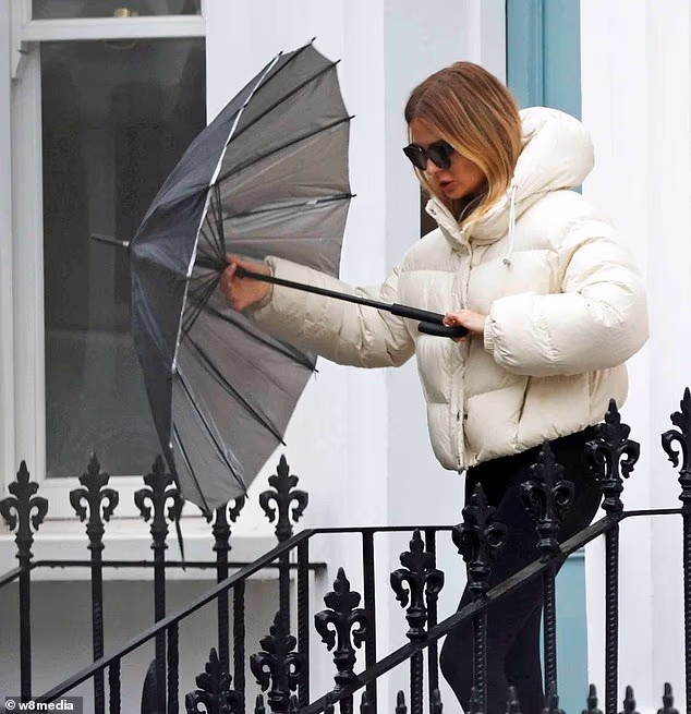 Millie se kišobranom sklonila od kiše dok je izlazila u bijeloj podstavljenoj jakni, crnim tajicama i Nike tenisicama