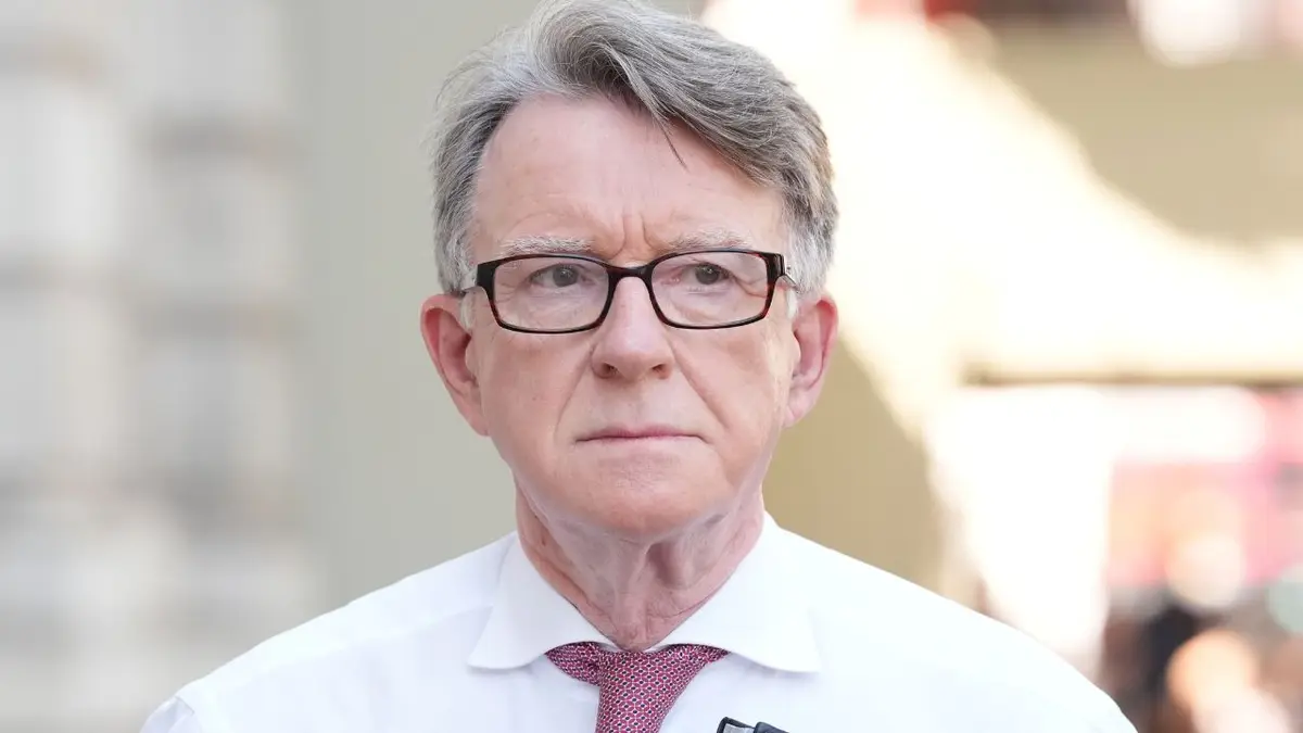 Peter Mandelson šeta vani noseći fascikl dok nosi naočale i crvenu kravatu