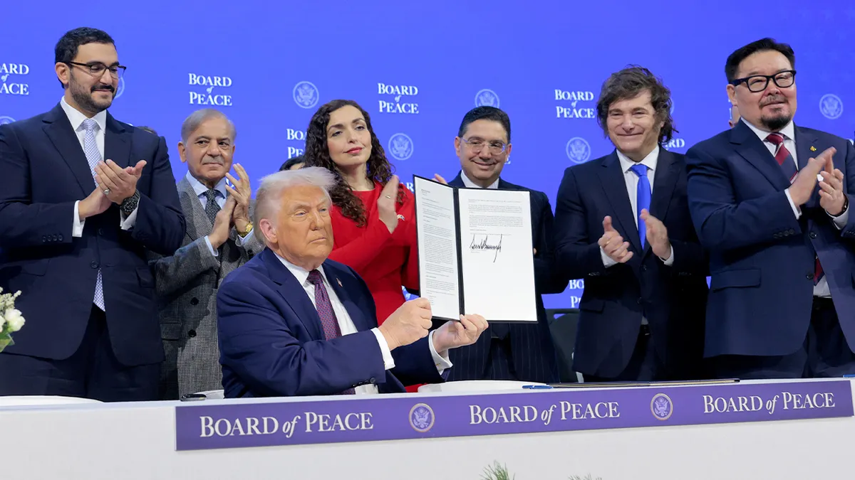 Američki predsjednik podiže potpisani dokument tijekom službenog diplomatskog događaja na međunarodnom forumu.