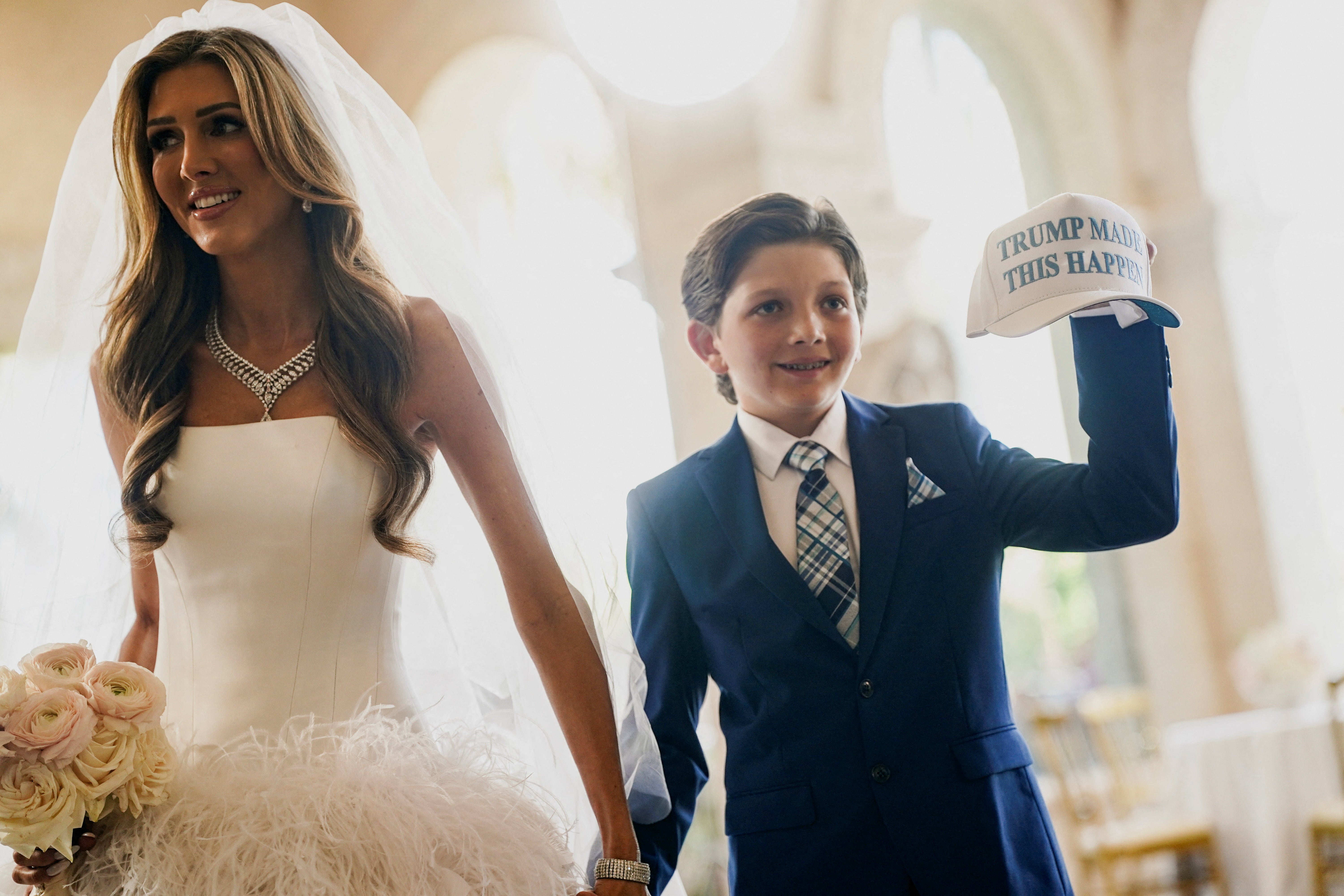 Erin Elmore, koja se udala za Dana Scavina na Trumpovom imanju Mar-a-Lago, drži se za ruke s djetetom koje pokazuje šešir na kojem piše: 'Trump je ovo učinio'