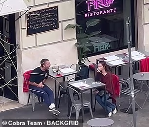 Žena naizgled nije bila uznemirena tim trenutkom jer je nastavila sjediti za malim stolom pokraj njega