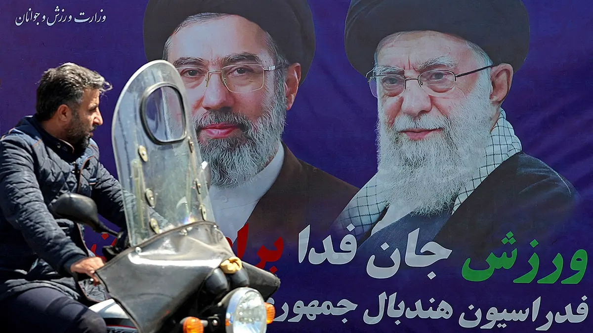 Vozač koji se vozi pored transparenta sa slikama ajatolaha Ali Khameneija i Mojtabe Khameneija u Teheranu