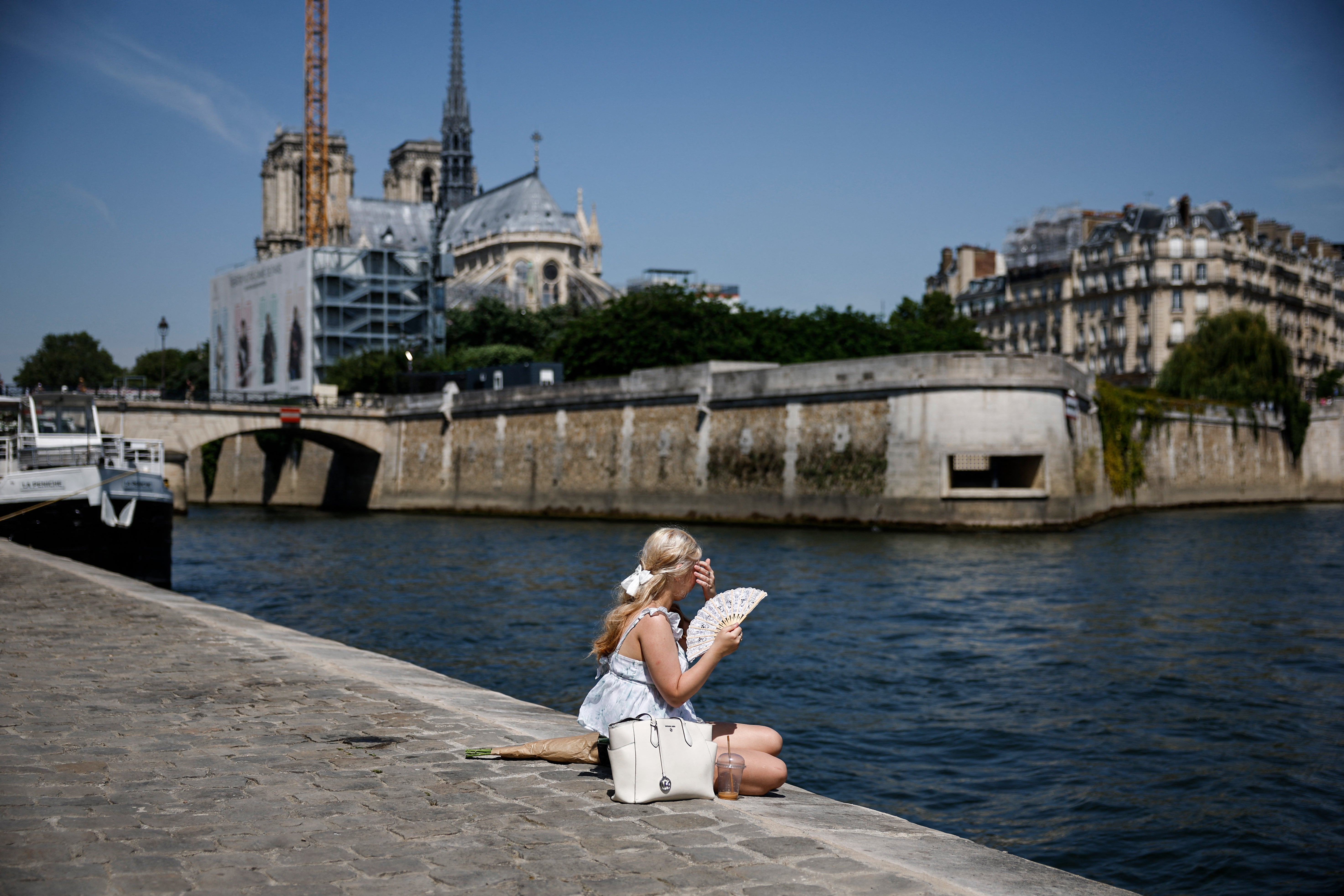 Žena sjedi na obalama rijeke Seine iza katedrale Notre-Dame u Parizu dok rekordno jak toplinski val prži dio zapadne Europe 28. svibnja