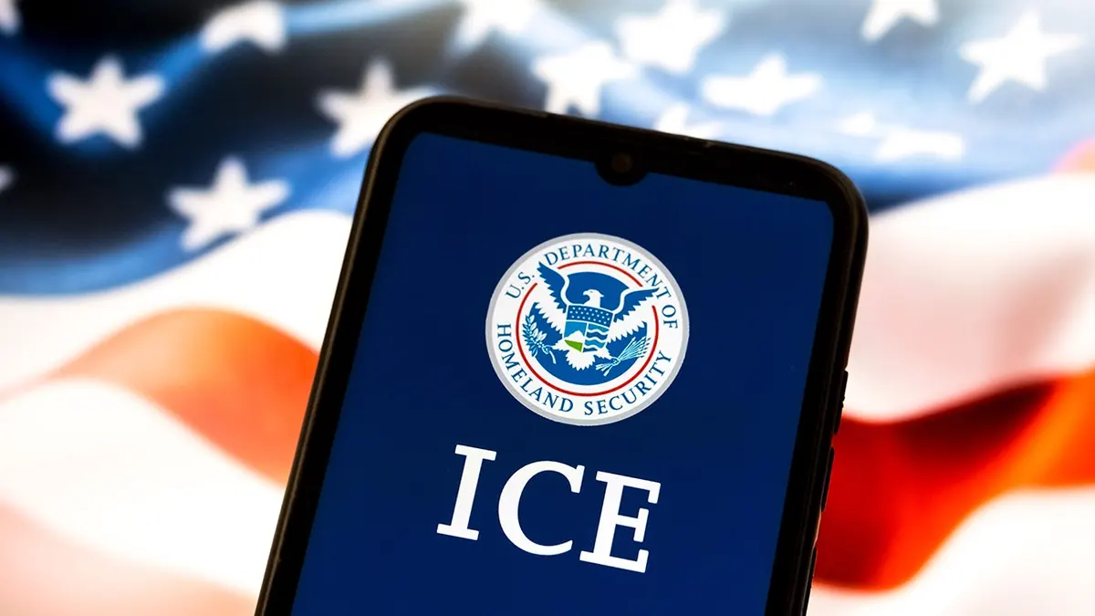 Pametni telefon prikazuje amblem američkog Ministarstva domovinske sigurnosti i ICE sa zastavom SAD-a na zaslonu prijenosnog računala iza