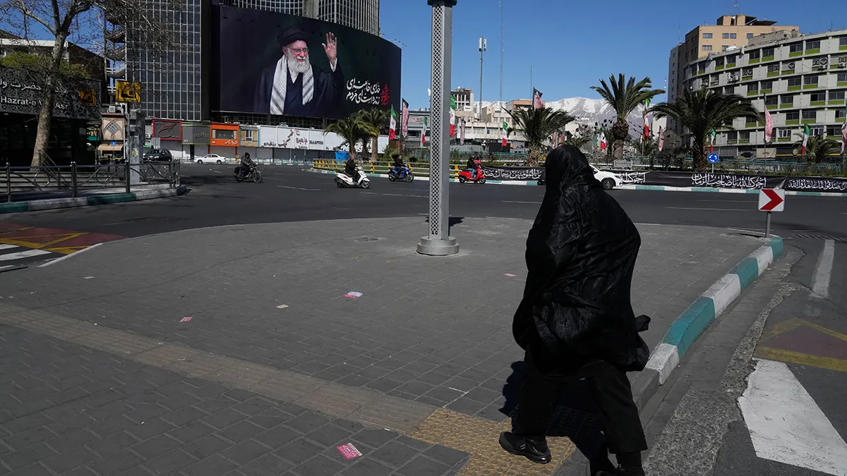 Žena hoda gotovo praznim javnim trgom s velikim jumbo plakatom ajatolaha Ali Khameneija u pozadini