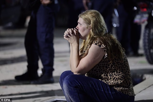 Žena se vidi kako plače ruku stisnutih dok prolaznici prebiru po ruševinama