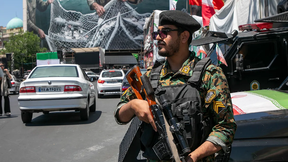 Iranski policajac stoji u patroli pokraj postera koji prikazuje iranske vojnike i američke vojne zrakoplove u Teheranu