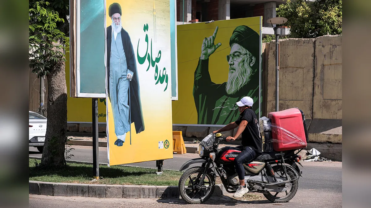 Dostavljač vozi motocikl cestom u Bagdadu pokraj reklamnih panoa Alija Khameneija i Hassana Nasrallaha