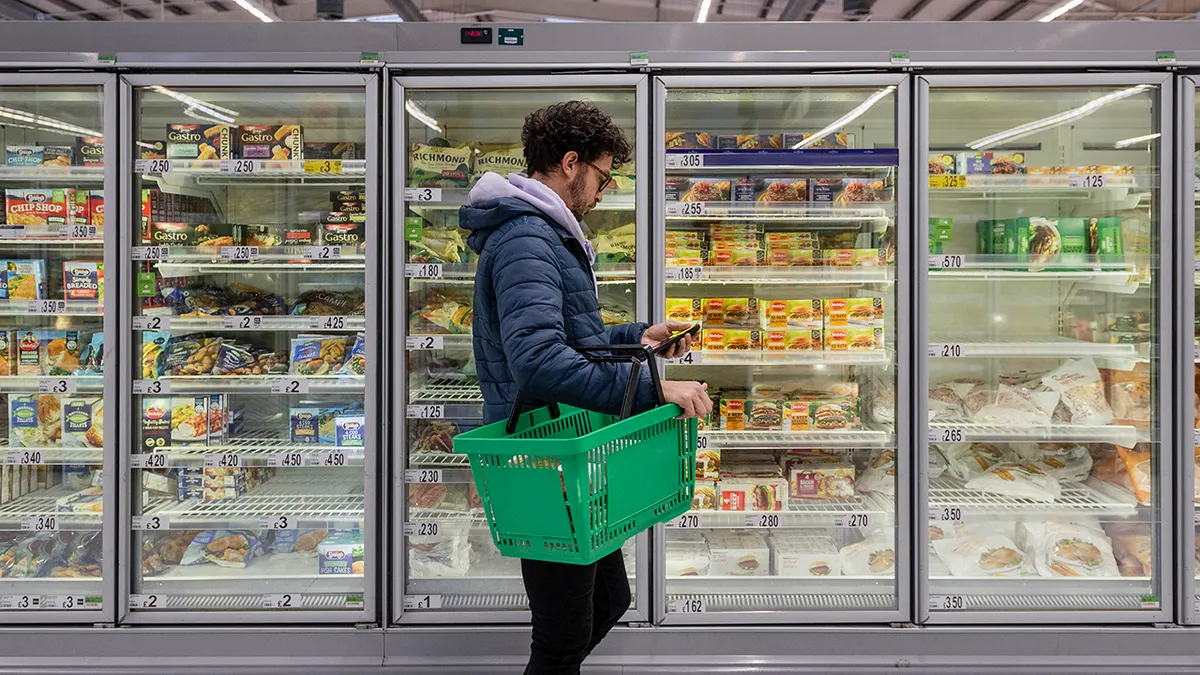 Čovjek stoji ispred zamrzivača supermarketa i gleda u svoj telefon