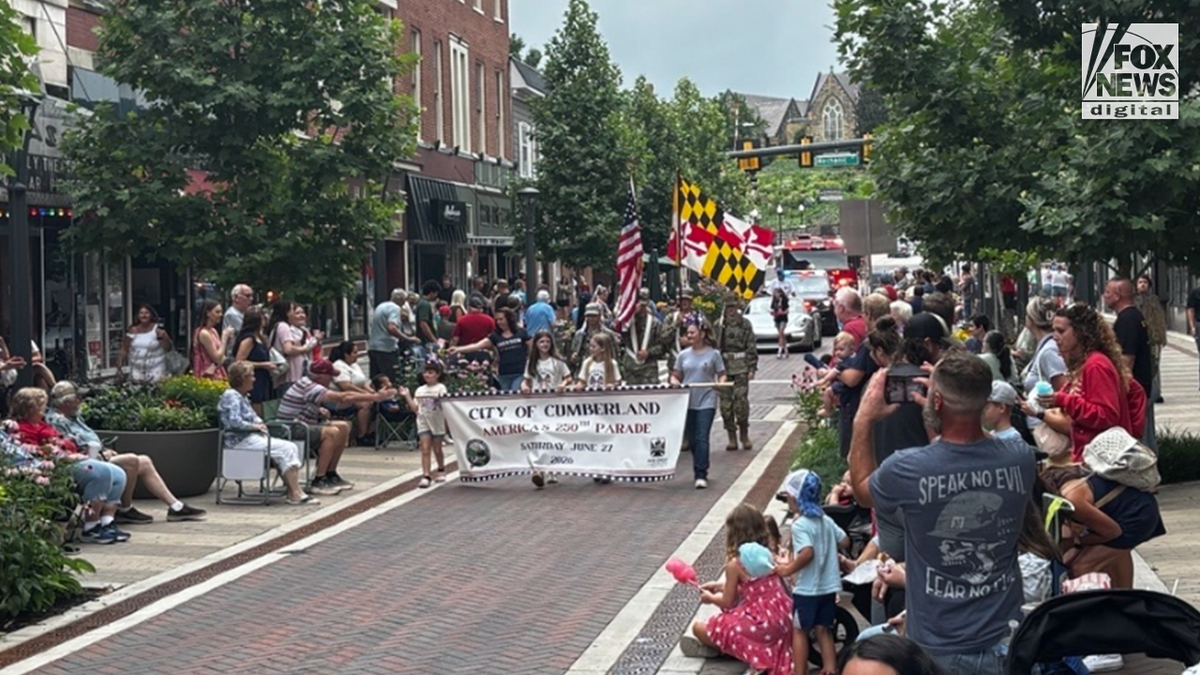 Sudionici parade nose transparent City of Cumberland America 250 i američke zastave i zastave Marylanda kroz središte Cumberlanda, Maryland, dok se gledatelji nalaze u nizu s obje strane ulice.