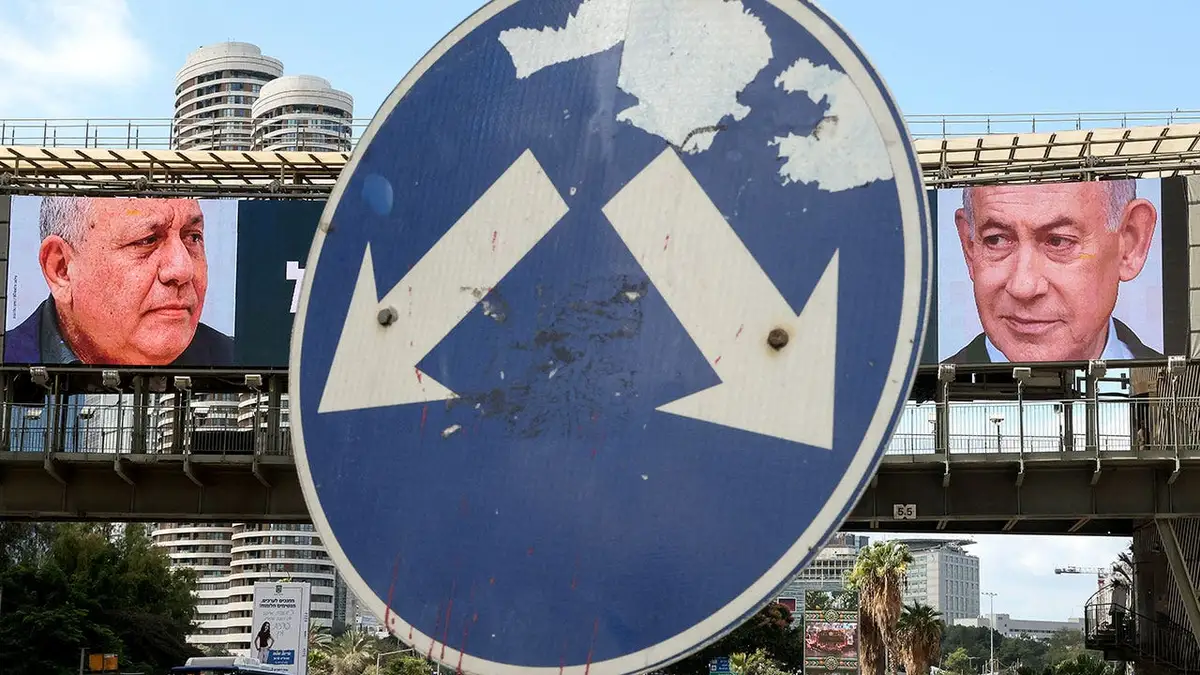 A road sign stands in front of a large billboard featuring Israel's Prime Minister Benjamin Netanyahu (R) of the Likud party and former military chief and leader of the centrist Yashar party, Gadi Eisenkot